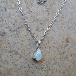 May include: A silver chain necklace with a teardrop-shaped opal pendant.