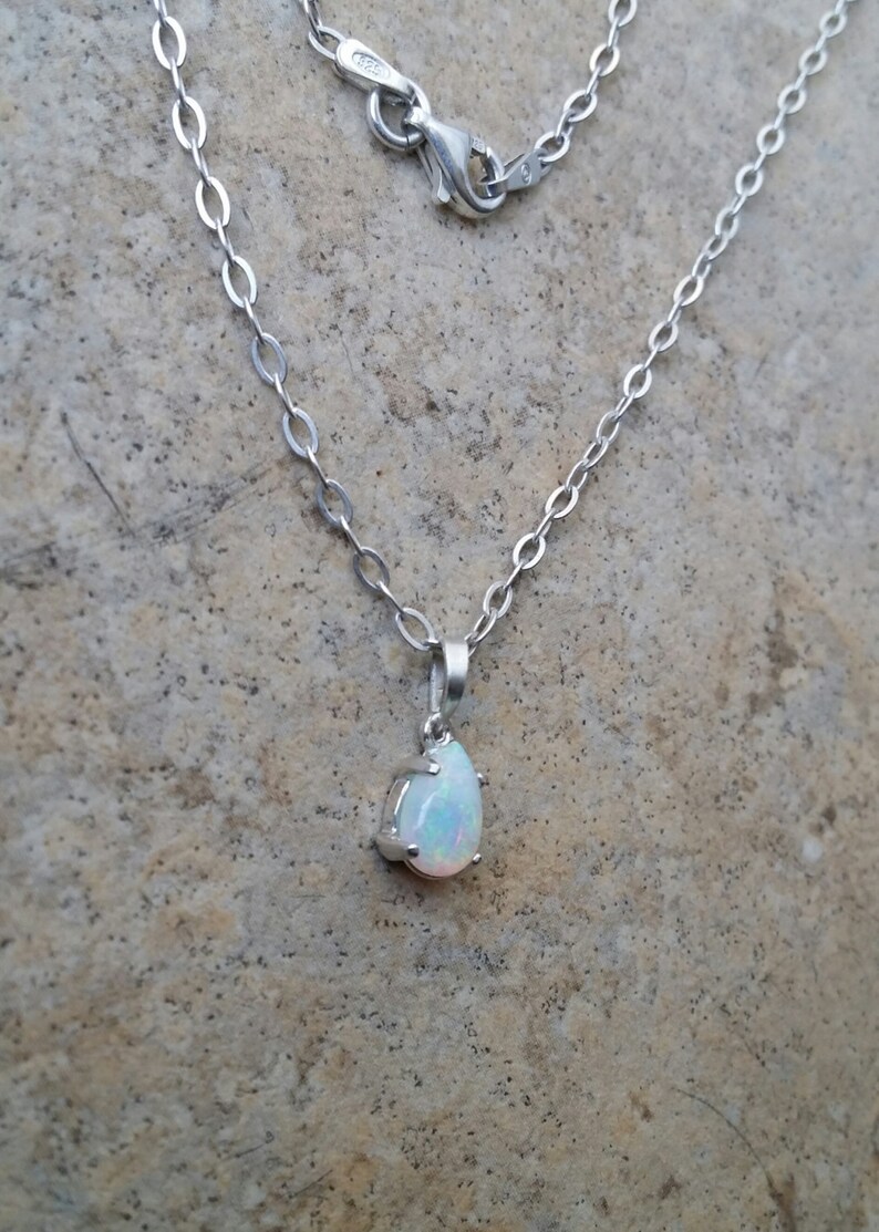 May include: A silver chain necklace with a teardrop-shaped opal pendant.