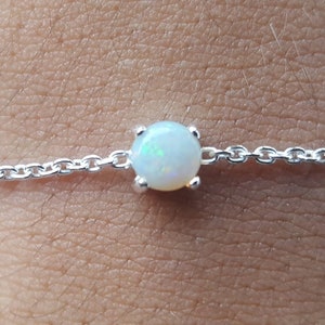 May include: A delicate silver chain bracelet with a single white opal gemstone.