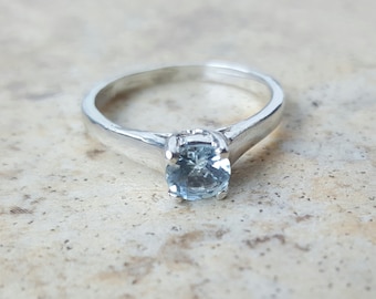 Pode incluir: Um anel de prata com uma gema azul claro.
