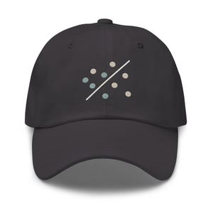 Puede incluir: Gorra de béisbol gris oscuro con visera curva. La gorra presenta un diseño bordado de pequeños círculos en tonos azules, beige y blancos, divididos por una línea diagonal blanca. Un accesorio casual.