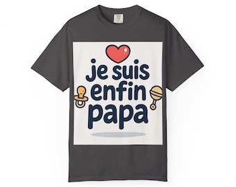 May include: Dark grey t-shirt with a white square graphic. The graphic features the text "je suis enfin papa" in dark blue, with a red heart, a pacifier, and a rattle. A cute gift for a new dad.