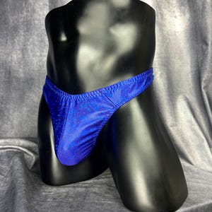 Op de afbeelding: Een blauwe, bedrukte zwembroekbodem wordt getoond op een zwarte mannequin. De zwembroek heeft een lage taille en een stringrug. De stof heeft een subtiele, getextureerde uitstraling.