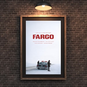 Könnte beinhalten: Gerahmtes Filmplakat für "Fargo" mit einem braunen Holzrahmen. Das Plakat zeigt den Titel in Rot, die Namen der Schauspieler und eine Szene mit einem Polizeiauto in einer verschneiten Landschaft. Das Plakat hängt an einer Backsteinmauer.