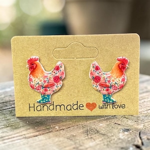 May include: A pair of chicken-shaped earrings with floral patterns and blue boots, displayed on a brown card. The card reads "Handmade with love" in black text, with a red heart symbol.