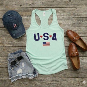 USA Flag Tank Top, perfect for the 4th of July and summer celebrations. This patriotic red, white, and blue tank top features the American flag design, ideal for Independence Day festivities. Whether you’re attending a parade or a BBQ, this tank is the perfect way to showcase your American pride. A thoughtful gift for anyone who loves to celebrate the USA!