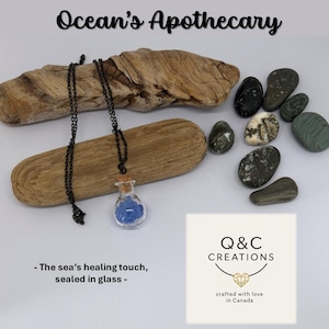 May include: A necklace featuring a small glass bottle pendant filled with blue material. The bottle has a cork stopper and hangs from a black chain. The text "Ocean's Apothecary" is at the top. The text "The sea's healing touch, sealed in glass" is at the bottom.