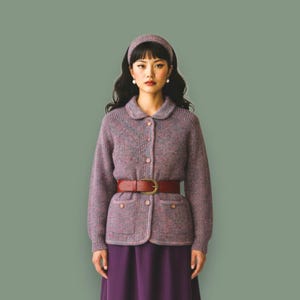 Peut inclure: Une femme porte une tenue d'inspiration vintage. L'ensemble comprend un cardigan mauve boutonné avec un col rond, un bandeau assorti et une ceinture bordeaux. La tenue est complétée par une jupe violette.