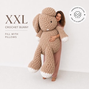 Pode incluir: Um coelho de crochê XXL feito de fio grosso castanho claro com detalhes brancos nas patas e orelhas. O coelho apresenta olhos de botão pretos e um pequeno nariz branco. O texto diz XXL CROCHET BUNNY FILL WITH PILLOWS e HANDMADE WITH LOVE.