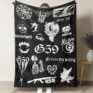 May include: Black blanket featuring multiple white graphic designs, including skulls, a skeleton, and the text "Suicideboys" and "G59". The blanket has a soft, velvety texture and is held up by a person.