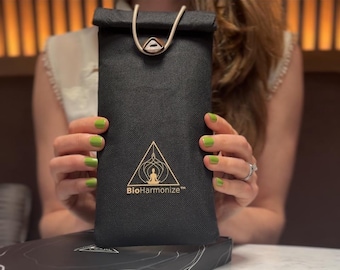 May include: A black pouch with a gold-colored logo and the text "BioHarmonize". The pouch has a cream-colored drawstring and a gold-colored clasp. The pouch is held by a person with green nail polish.