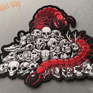 May include: Embroidered patch with a black border, depicting a pile of skulls and bones, encircled by a large red centipede. The text "THAT KILT GUY" is arched across the top of the patch.