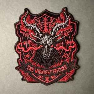 May include: An embroidered patch featuring a black and red design of a horned creature with glowing red eyes. The circular background includes intricate red line work and symbols. A banner at the bottom displays the text THE MIDNIGHT EPICURE.