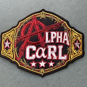 May include: A black embroidered patch featuring the text ALPHA CARL in white with red outlines. The design includes a red anarchy symbol, barbed wire accents, and five white stars set against a gold and black decorative border.