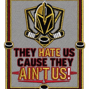 May include: A rectangular embroidered patch with a grey background and a gold, black, and white border. The design features a knight helmet emblem, crossed hockey sticks, and hockey pucks. The text reads: THEY HATE US CAUSE THEY AIN'T US!