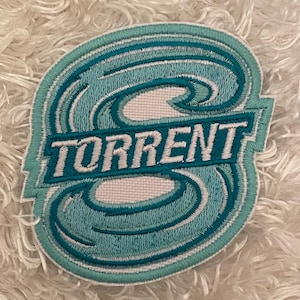 May include: Embroidered patch with the word "TORRENT" in white block letters. The patch features a stylized wave design in shades of teal and light blue, outlined in white and teal. The patch is on a white, fluffy surface.