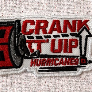 May include: Embroidered patch with the words "CRANK IT UP HURRICANES" in red and black. The patch features a stylized design of a weight and an arrow pointing upwards, all outlined in white.