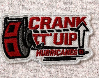 以下が含まれることがあります： 赤と黒で「CRANK IT UP HURRICANES」の文字が刺繍されたパッチ。パッチは、ウェイトと上向きの矢印の様式化されたデザインを特徴とし、すべて白で縁取られています。