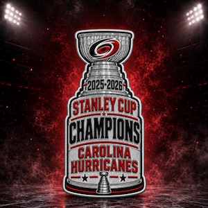 May include: A silver-toned Stanley Cup trophy graphic featuring the text 2025-2026, STANLEY CUP CHAMPIONS, and CAROLINA HURRICANES in black and red lettering, with the Carolina Hurricanes logo at the top and a small trophy icon at the bottom.