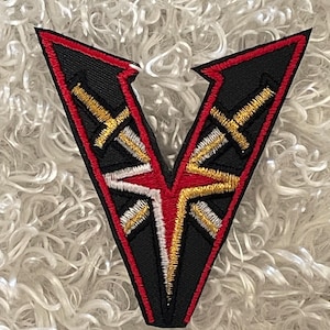 May include: Black and red embroidered patch with a gold V shape and a cross design.