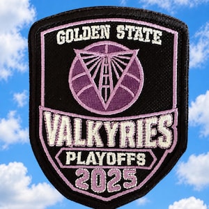 May include: A shield-shaped embroidered patch with a black background and light purple stitching. It features the text GOLDEN STATE, VALKYRIES, PLAYOFFS, and 2025 in white and purple, with a central graphic of a basketball and a bridge structure.