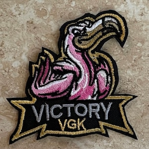 May include: Embroidered patch featuring a pink flamingo with a gold beak and a banner that reads "VICTORY VGK".