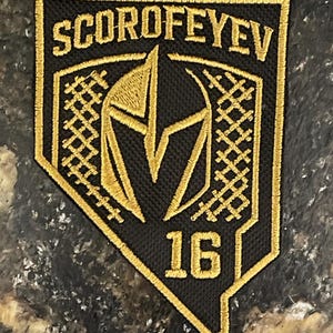 May include: Black and gold embroidered patch with the name SCOROFEYEV and the number 16. The patch features a shield design with a gold gladiator helmet in the center and gold border.