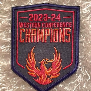 May include: A navy blue and red patch with the text "2023-24 WESTERN CONFERENCE CHAMPIONS." The patch features a stylized orange and red phoenix rising from flames. The patch has a dark blue border.