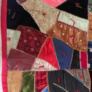 May include: A patchwork quilt made of various fabrics in shades of red, brown, green, blue, and pink. The quilt is stitched together with gold thread and has a variety of patterns, including paisley, polka dots, and geometric designs.