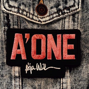 May include: A black embroidered patch with the words "A'ONE" in red thread and the signature "Aja Wil" in white thread. The patch is set against a denim jacket.