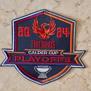 May include: A navy blue, red, orange, and white embroidered patch with a phoenix logo and the text "2024 Firebirds Calder Cup Playoffs".