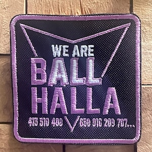 May include: Square black patch with a purple border and text. The text reads "WE ARE BALL HALLA" in purple, with phone numbers below. The patch has a textured appearance.