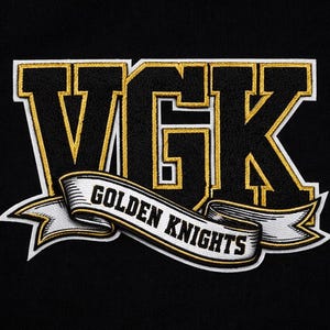 May include: Embroidered patch featuring the letters "VGK" in black and gold, with a white outline. A banner below reads "GOLDEN KNIGHTS" in black lettering. The patch is on a black background.