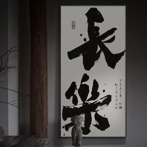 May include: A framed artwork with striking black calligraphy on a white backdrop. The piece showcases two large characters, accompanied by smaller text and a red seal in the upper right. A small statue is positioned in front.