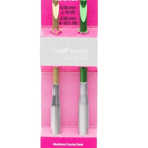 May include: A package of two aluminum crochet hooks. One hook has a gold-colored head and the other has a green-colored head. The package is pink and has the brand name "Susan Bates" and the size of the hooks printed on it.