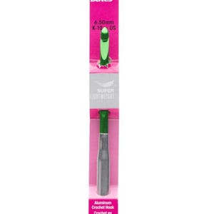 May include: A Susan Bates aluminum crochet hook, size 6.50mm (US K-10), with a green handle and silver shaft. The hook is packaged on a pink and white card with the brand name and product details.