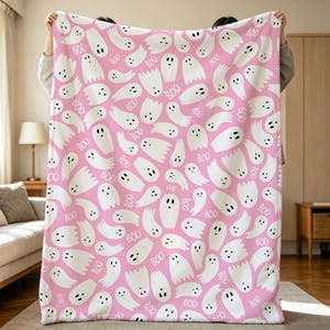 Può includere: Una morbida coperta con un motivo ripetuto di fantasmi bianchi con occhi e bocche neri su uno sfondo rosa acceso. Il design include la parola BOO stampata in bianco e sparsa tra i fantasmi su tutta la superficie del tessuto.