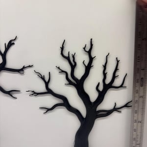May include: Two black, flat, silhouette-style tree cutouts with bare, spindly branches. A metal ruler is positioned vertically next to the trees, showing the taller tree measures approximately 14 cm in height from base to top.