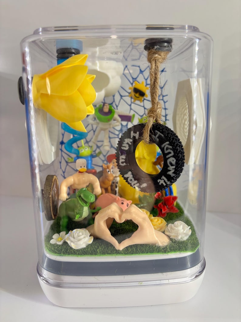 May include: A clear rectangular display case containing various miniature toy figures, including a green dinosaur, a pig, and a space ranger. A black tire ornament hangs from a jute rope with the text I knew it roll written in white paint.