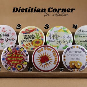 May include: A collection of seven round Dietitian Corner buttons with various designs and text. The buttons feature phrases like "Girl Dinner," "I'm nacho average dietitian," and "Fad Diet Fighters." The buttons are white, yellow, red, and blue.