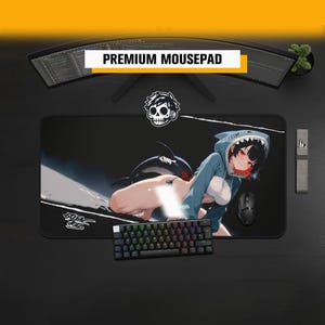May include: A rectangular black mousepad featuring an anime-style character wearing a blue shark-themed hoodie. The design includes a white skull icon, a shark silhouette, and stylized text. A black mechanical keyboard and mouse sit on the pad.