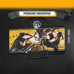 Puede incluir: Una alfombrilla de ratón rectangular con una ilustración gráfica en amarillo y negro de un personaje estilo anime con cabello rubio y máscara negra. El diseño incluye salpicaduras de tinta negra, un icono de calavera y el texto "TRIGGER".