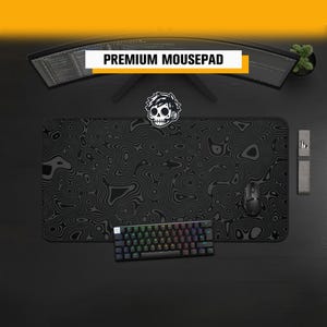 Puede incluir: Una alfombrilla de ratón rectangular negra con un patrón de líneas de contorno topográficas gris oscuro y un gráfico de calavera blanca en el centro. La alfombrilla se sitúa bajo un monitor curvo con un ratón y teclado negros.