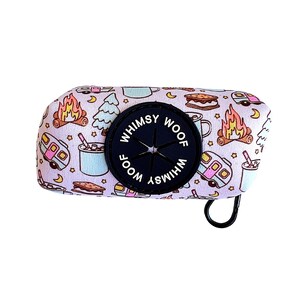 May include: A light purple dog waste bag dispenser with a camping theme. The dispenser features a black rubber outlet with the words "Whimsy Woof" in white. The bag has a repeating pattern of campfires, trees, and camper vans.