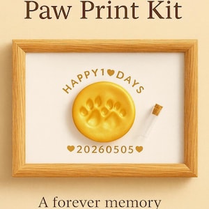 May include: Custom Paw Print Kit in a wooden frame. The kit includes a golden paw print impression, a small vial, and the text "HAPPY 1 DAYS" and "20260505". The text "A forever memory for your beloved pet" is also included.