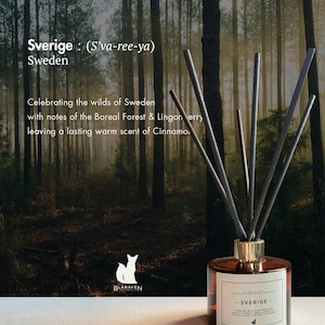 May include: A reed diffuser with a round amber glass bottle and a white label featuring the text Sverige, Blaraven, and scent notes. Five dark grey reeds extend from a gold-toned collar. The background shows a forest scene with tall trees.