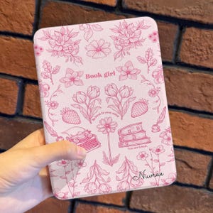 Op de afbeelding: Een roze tablethoesje met een bloemenpatroon en de woorden "Book girl". De hoes bevat illustraties van bloemen, aardbeien, een typemachine en boeken. De tekst "Be kind to your mind" en "You are loved" is ook opgenomen.