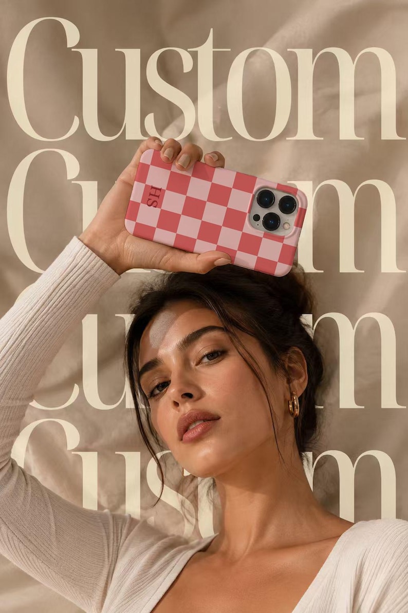 May include: A rectangular smartphone case featuring a pink and white checkered pattern. The case includes a camera cutout on the upper right side and the letters SH printed in a small, dark font on the upper left side of the checkered surface.