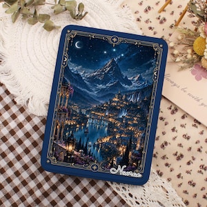 May include: A rectangular dark blue tin box featuring a detailed illustration of a mountain landscape at night with a glowing town, a river, and a crescent moon. The frame has gold decorative accents and the word Navrae printed in white script.