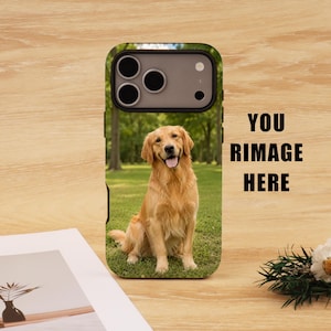 Op de afbeelding: Een telefoonhoesje met een foto van een golden retriever hond die op gras zit. De hoes heeft een zwarte rand en de tekst "YOU RIMAGE HERE" in het zwart. De hond is lichtbruin.